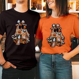 May include: A black t-shirt and an orange t-shirt, each featuring a central graphic of a ghost shape filled with a patchwork pattern of pumpkins, bats, and smaller ghosts. The ghost graphic is topped with a bow and has two large black oval eyes.