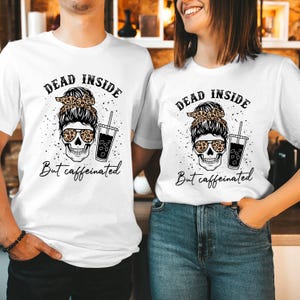 May include: Two white t-shirts featuring a graphic of a skull with a messy bun, leopard print headband, and leopard print sunglasses. The skull holds an iced coffee. The text reads DEAD INSIDE But caffeinated in black lettering.