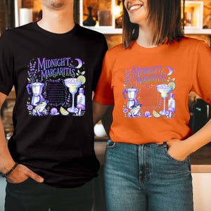 May include: A black t-shirt and an orange t-shirt, each featuring a graphic print with the text Midnight Margaritas, a cocktail glass, a moka pot, a frog wearing a witch hat, a snail, a mushroom, lavender sprigs, and a crescent moon.