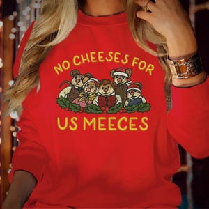 Peut inclure: Un sweat-shirt rouge à manches longues avec une broderie représentant quatre souris vêtues de vêtements d'hiver au-dessus d'une guirlande de houx. Le texte jaune au-dessus indique NO CHEESES FOR et en dessous US MEECES en lettres rondes.