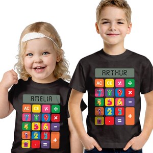 May include: Two black t-shirts featuring calculator designs. One shirt displays "AMELIA" above colourful calculator buttons. The other shirt shows "ARTHUR" above a similar calculator design. Both shirts have numbers and mathematical symbols.