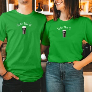 Op de afbeelding: Twee mensen dragen bijpassende groene t-shirts. De shirts hebben de tekst "Split The G" boven een afbeelding van een donkere pint bier met de letter "G" erin. De shirts hebben een effen, heldergroene kleur.
