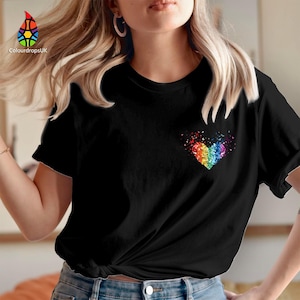 Pode incluir: T-shirt preto com um design de coração arco-íris no peito. O coração é composto por pequenas formas coloridas. A t-shirt tem mangas curtas e gola redonda. O logótipo da marca está no canto superior esquerdo.