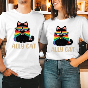 May include: White t-shirts featuring a black cat design wearing rainbow sunglasses and a rainbow cape. The text "ALLY CAT" is printed below the cat. The shirts are worn by two people.