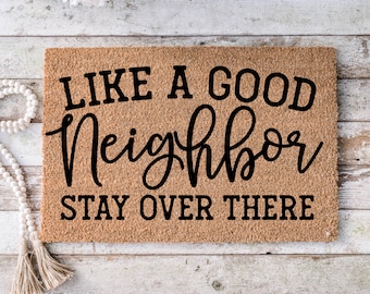 Puede incluir: Una alfombra de coco marrón con el texto "Like a good neighbor stay over there" en letras negras.