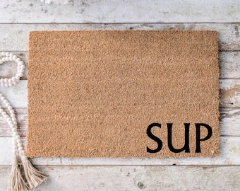May include: A brown coir doormat with the word "SUP" in black lettering.
