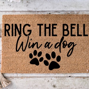 May include: A brown coir doormat with the text "RING THE BELL Win a dog" in black lettering. Two black paw prints are below the text.
