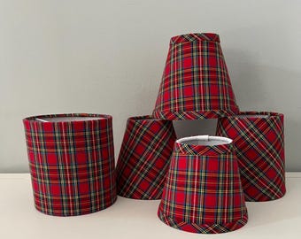 May include: A collection of five fabric lampshades featuring a red, green, yellow, and blue plaid pattern. The set includes one cylindrical shade and four tapered shades of varying sizes, all with finished edges and a white interior lining.