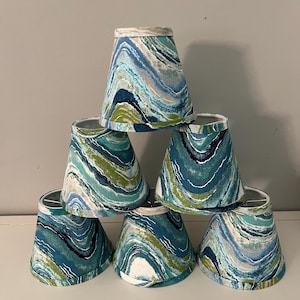 May include: Six blue and green patterned lampshades with a white background. The lampshades are stacked in a pyramid shape.