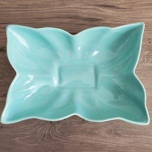 May include: A light blue, ceramic serving dish with a unique, four-lobed shape. The dish has a rectangular center and gently curved edges. The glossy finish reflects light, highlighting the smooth surface. This decorative piece is ideal for serving snacks or small dishes.