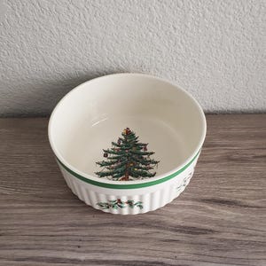 May include: White ceramic bowl with a green and red Christmas tree design. The bowl has a ribbed exterior with a green stripe and holly accents. A festive piece for serving holiday dishes.