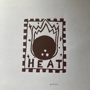 May include: A brown and white print of a stylized image of a ball with flames on top. The word "HEAT" is printed below the ball. The print is framed with a checkered border.