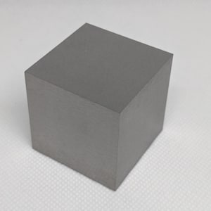 Könnte beinhalten: Ein massiver, grauer Würfel mit mattem Finish. Der Würfel ist ein perfektes Quadrat, wobei alle Seiten gleich sind. Die Oberfläche scheint glatt und gleichmäßig zu sein. Der Würfel ist eine einfache geometrische Form.