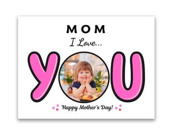 May include: A white Mother's Day card with the word "MOM" above "I Love... YOU". The word "YOU" is in pink with a black outline, framing a photo of a smiling child. The text "Happy Mother's Day!" is below.