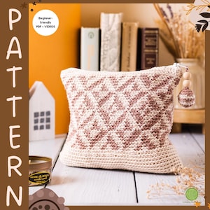 Puede incluir: Un cojín de ganchillo color crema con un patrón geométrico en tonos marrones. El cojín tiene un cierre de cremallera con un dije de cuentas de madera y bola de ganchillo. La imagen también incluye el texto "PATTERN" y "Beginner-friendly PDF + VIDEOS".