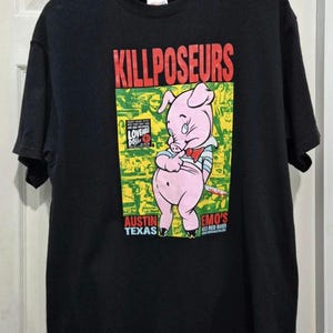 Może przedstawiać: Czarny t-shirt z kreskówkową świnią trzymającą nóż. Koszulka ma czerwony napis "KILLPOSEURS", a także "AUSTIN TEXAS" i "EMO'S 603 RED RIVER". Świnia ma na sobie muszkę i koszulę w paski.