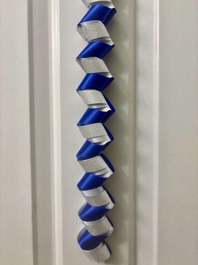 Puede incluir: Una guirnalda decorativa vertical con un patr&oacute;n de espiral repetitivo que alterna cinta de sat&eacute;n azul real y cinta de purpurina plateada. Las cintas est&aacute;n trenzadas para crear una estructura continua en forma de sacacorchos.