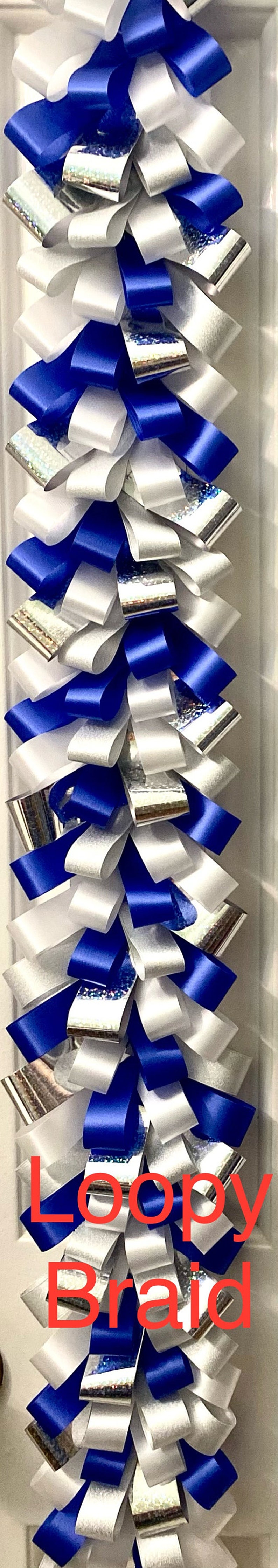 Puede incluir: Una decoraci&oacute;n de trenza de bucles vertical construida con bucles alternos de cinta azul real s&oacute;lida, cinta blanca s&oacute;lida y cinta hologr&aacute;fica plateada. Las cintas est&aacute;n superpuestas y dobladas para crear un patr&oacute;n denso, texturizado y repetitivo.