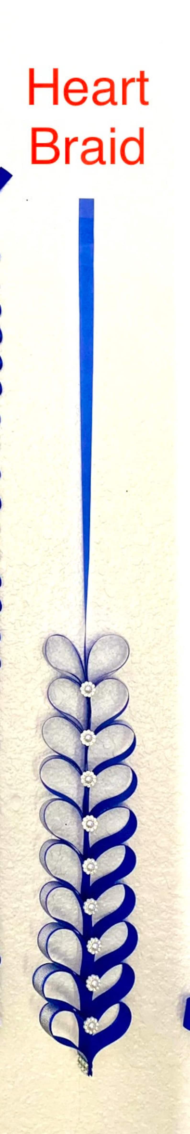 Puede incluir: Una cinta azul vertical titulada Heart Braid. La cinta est&aacute; doblada en una serie de formas de coraz&oacute;n repetitivas dispuestas en columna. Cada intersecci&oacute;n de coraz&oacute;n est&aacute; acentuada con un peque&ntilde;o adorno floral blanco, redondo y texturizado.