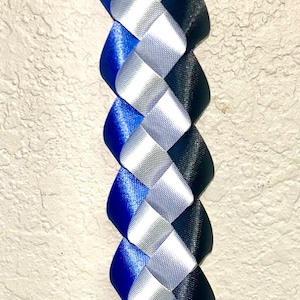 Puede incluir: Una trenza de cinta decorativa larga que presenta un patr&oacute;n repetitivo de cintas de sat&eacute;n azul real, plateado y negro tejidas juntas en un dise&ntilde;o en espiral apretado y entrelazado que crea una hebra vertical continua, texturizada y multicolor.