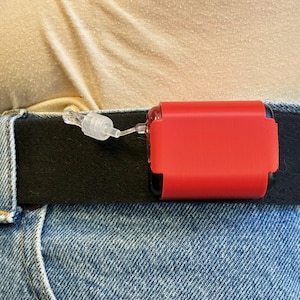 Può includere: Un dispositivo medico rosso attaccato a una cintura nera con un tubo di plastica trasparente.