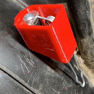 May include: A red plastic spring-loaded clip with a metal spring and a silver screw. The clip is attached to a metal wire.