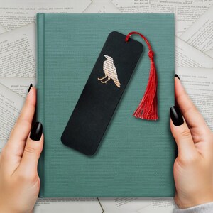 Handmade bookmark inspired by Edgar Allan Poe's poem The Raven. A raven shape cut from on each side of black card reveals a yellowed and aged section of text from the iconic horror classic, and is finished off with a silky red tassel.