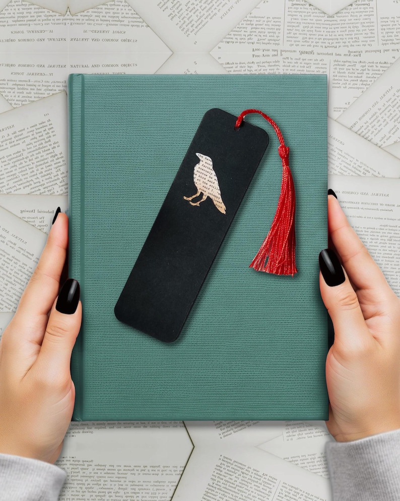 Handmade bookmark inspired by Edgar Allan Poe's poem The Raven. A raven shape cut from on each side of black card reveals a yellowed and aged section of text from the iconic horror classic, and is finished off with a silky red tassel.