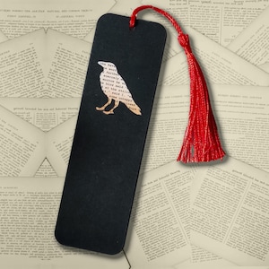 May include: A rectangular black bookmark featuring a cutout silhouette of a raven filled with printed text from Edgar Allan Poe's The Raven. The bookmark includes a vibrant red cord tassel attached through a hole at the top center.