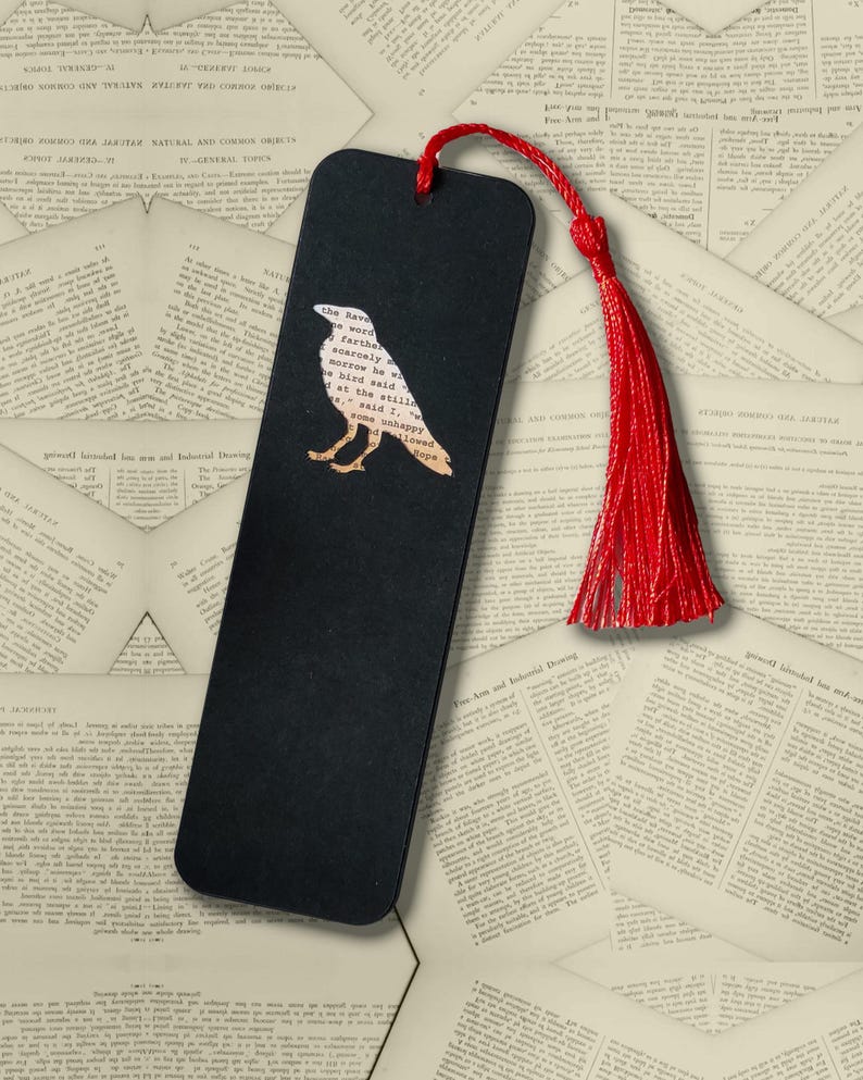 May include: A rectangular black bookmark featuring a cutout silhouette of a raven filled with printed text from Edgar Allan Poe's The Raven. The bookmark includes a vibrant red cord tassel attached through a hole at the top center.