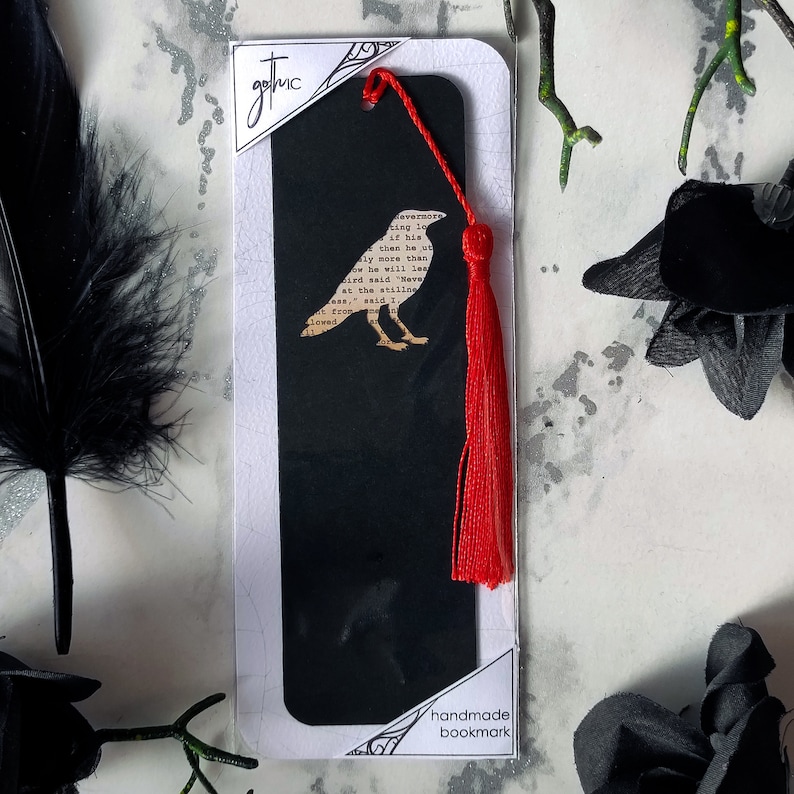 Handmade bookmark inspired by Edgar Allan Poe's poem The Raven. A raven shape cut from on each side of black card reveals a yellowed and aged section of text from the iconic horror classic, and is finished off with a silky red tassel.
