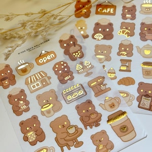 May include: A sheet of decorative stickers with brown bear characters and cafe-themed designs. Includes coffee cups, pastries, and the word "CAFE". The stickers have gold foil accents and the text "N.200 DECO KOLLECTION KOLOUR CAFE".
