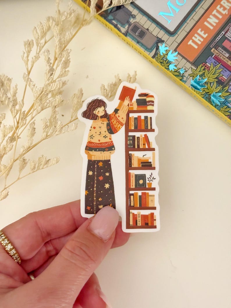 May include: A sticker featuring a cartoon illustration of a person in a floral patterned dress reaching for a book on a bookshelf filled with books. The bookshelf is brown with white shelves. The person is wearing a sweater with a floral pattern.