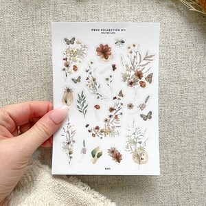May include: A sheet of stickers featuring watercolor illustrations of flowers, leaves, and butterflies in shades of brown, beige, and green. The stickers are labeled "Deco Kollektion N&deg;1 Koulour Cafe" and "DK1".