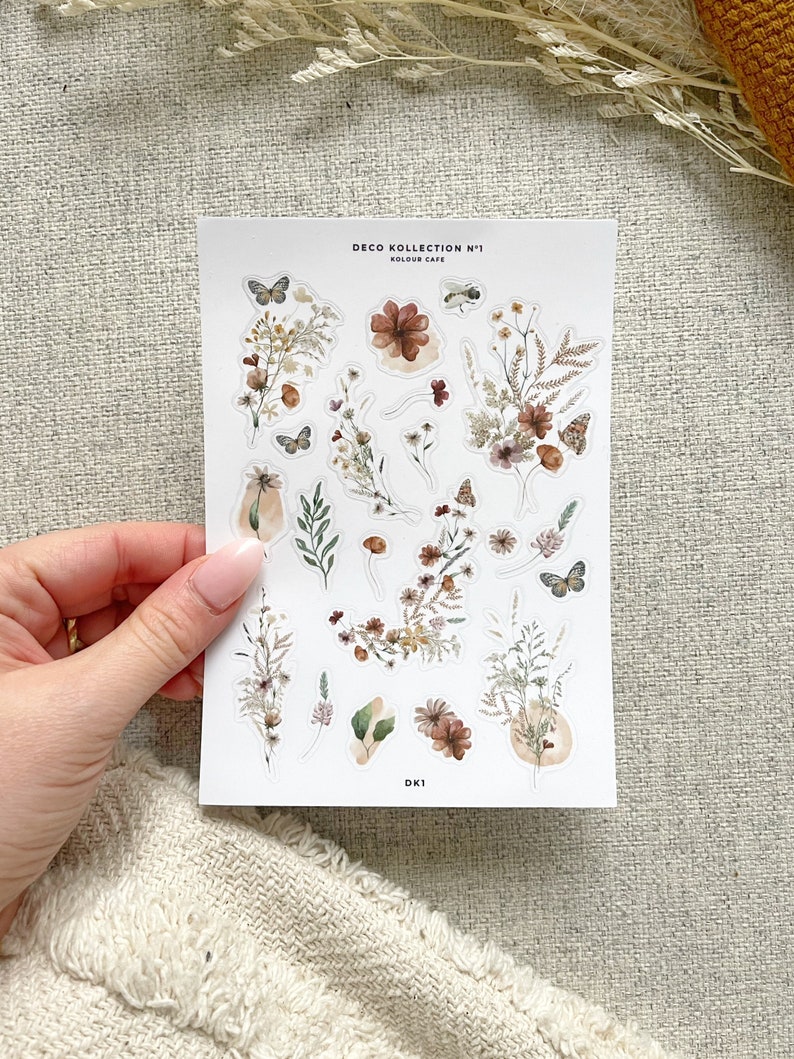 May include: A sheet of stickers featuring watercolor illustrations of flowers, leaves, and butterflies in shades of brown, beige, and green. The stickers are labeled "Deco Kollektion N&deg;1 Koulour Cafe" and "DK1".