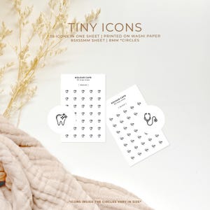 Puede incluir: Dos hojas de papel washi blanco con contornos negros de 35 iconos diminutos. Los iconos están dispuestos en una cuadrícula y están rodeados por círculos de 8 mm. Los iconos incluyen un diente con una estrella, un estetoscopio y otros iconos pequeños. El texto "KOLOUR CAFE" y "35 tiny icons" está impreso en cada hoja.