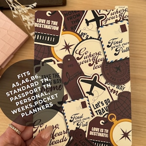Puede incluir: Una cubierta de planificador con temática de viajes, adornada con diseños tipo pegatina. Presenta imágenes de aviones, brújulas, etiquetas de equipaje y frases como "Love is the Destination" y "Find your own Path". El planificador se adapta a planificadores A5, A6, B6, Standard TN, Passport TN, Personal, Weeks y Pocket.