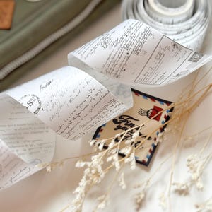 May include: A roll of white washi tape with black script writing. The tape is unrolled and the end of the roll is visible. The tape is on a white surface with a small white flower arrangement and a small card with the text "Find your happy place" in black script.