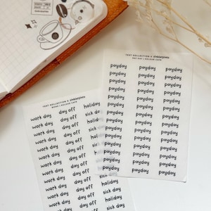 May include: Transparent sticker sheets with black text, including terms such as "payday," "work day," and "day off." These stickers are designed for use in planners and journals. A brown leather journal and coffee-themed stickers are also visible.
