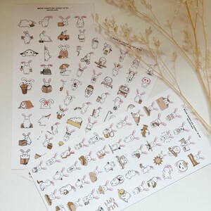 May include: Two sheets of stickers with cartoon bunnies in various poses. The stickers are mainly white with brown and pink details. Text on the sheets reads "BEAN SAMPLER SHEET N°01". The stickers are ideal for scrapbooking.