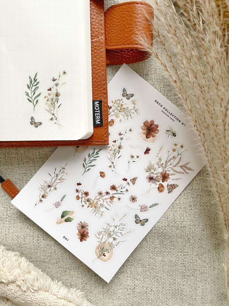 May include: A sheet of stickers featuring a floral design with butterflies. The stickers are on a white background and have a rustic, vintage aesthetic. The text "DECO KOLLECTION N&deg;1" and "KOLOUR CAFE" is printed on the sheet.