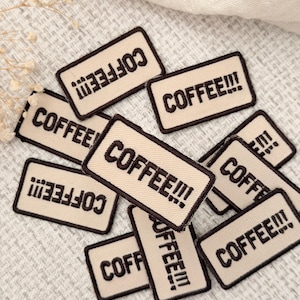 May include: A collection of rectangular embroidered patches featuring a beige background with a dark brown border and the text COFFEE!!! stitched in dark brown thread. The patches are arranged in a scattered pile, showcasing the consistent design.