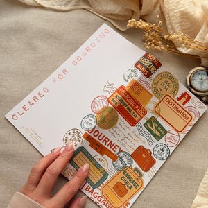 Pode incluir: Um cartão branco com selos temáticos de viagem e texto, incluindo "CLEARED FOR BOARDING", "JOURNEY" e "BAGGAGE CHECK". Os selos apresentam imagens de bagagem, um globo e vários destinos em laranja, vermelho e verde.