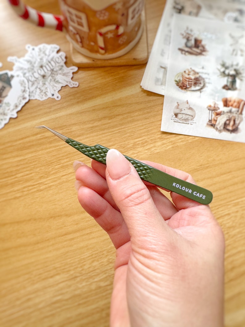 May include: Green tweezers with a slanted tip and a textured grip. The tweezers have the words "KOLOUR CAFE" printed on the side.