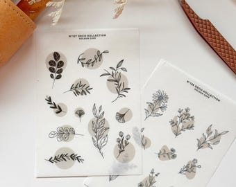 May include: Two sheets of clear sticker paper with black line drawings of leaves, flowers, and branches. The top sheet has the text "N°127 DECO KOLLECTION KOLOUR CAFE" and the bottom sheet has the text "N°128 DECO KOLLECTION KOLOUR CAFE".