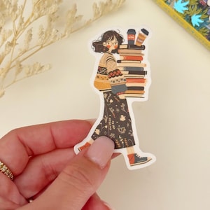 May include: A sticker of a cartoon woman wearing a brown and white sweater and a black skirt with a floral pattern. She is carrying a stack of books and two coffee cups.