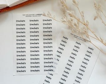 May include: Two sheets of white stickers with black text. One sheet says "trackers" repeatedly, and the other says "tasks." The stickers are from the "TEXT KOLLECTION x stebierpi TRACKERS | KOLOUR CAFE" collection.