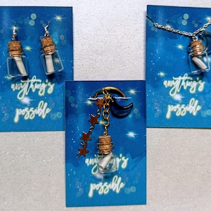 May include: A selection of handcrafted jewellery items: earrings, a necklace, and a keyring. Each piece features a small glass bottle with a cork, holding a rolled message. The background is a blue card with the text "anything's possible".