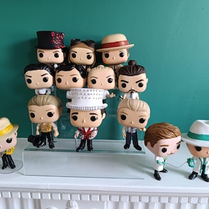 May include: A collection of 12 colorful pop vinyl figures, some wearing hats, arranged on a glass shelf. The figures are all different and have unique features.