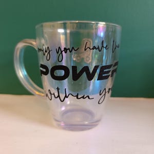 May include: Iridescent glass mug with a handle. The mug features the words "may you have the POWER within you" in black lettering. A small roller skate graphic is also visible. The mug is on a white surface with a green background.